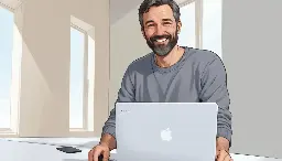 Un hombre caucásico de mediana edad con barba y cabello rizado, vestido con un suéter gris, sentado en un escritorio y usando una computadora portátil
